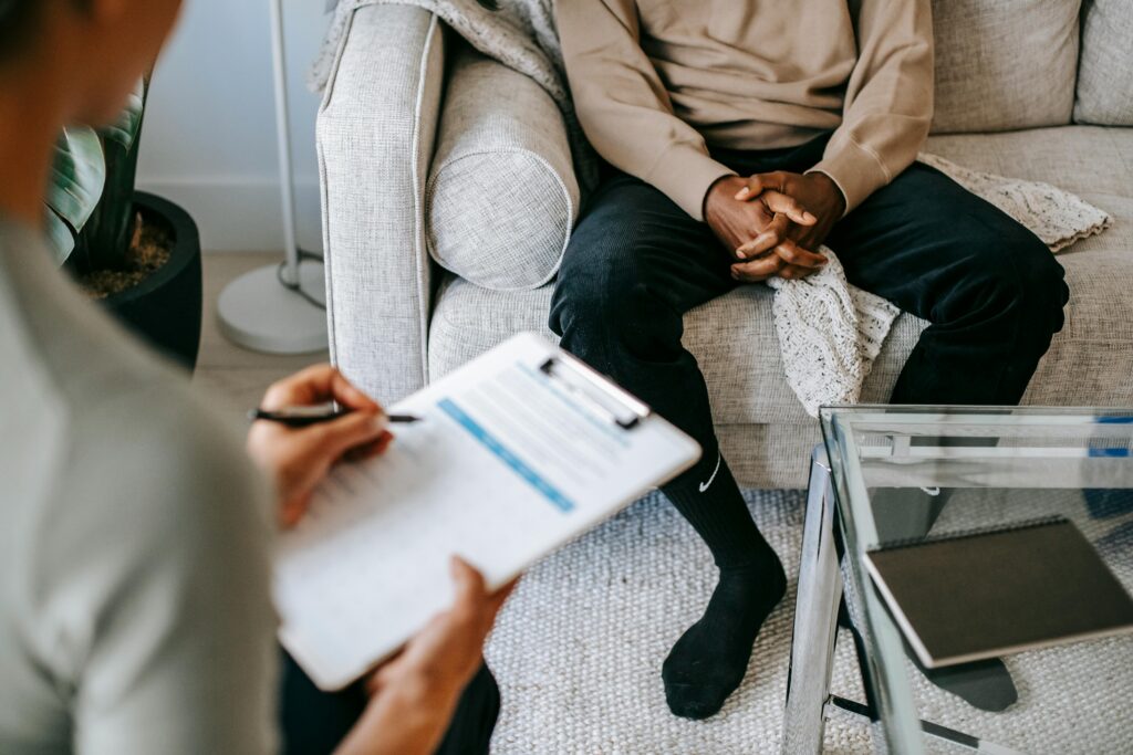 pexels-photo-5699431-5699431 Therapist takes notes as client sits on a sofa during a psychotherapy session.